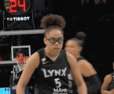 A Woman Wearing A Lynx 5 Jersey Stands In Front Of A Scoreboard GIF