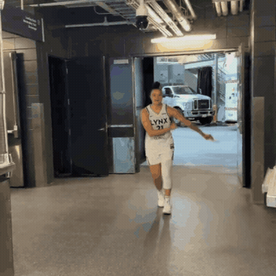 A Woman Wearing A Lynx Jersey Is Walking Down A Hallway GIF