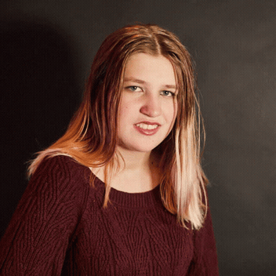 A Woman Wearing A Maroon Sweater Is Smiling And Looking At The Camera GIF