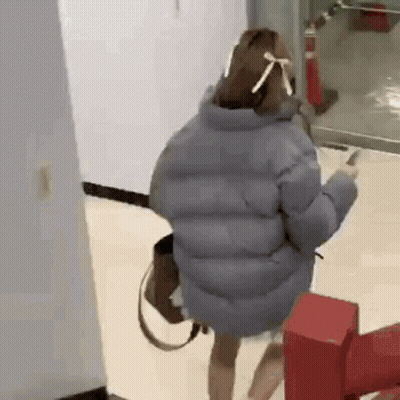 A Woman Wearing A Mask And A Jacket Is Standing In A Hallway . GIF