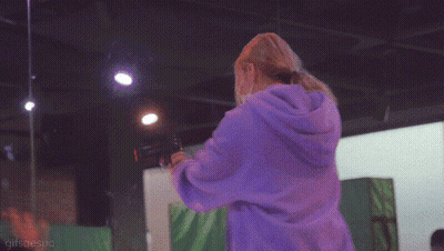 A Woman Wearing A Mask And A Purple Hoodie Is Standing In A Room GIF
