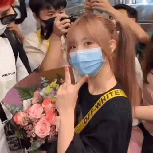 A Woman Wearing A Mask Is Giving The Middle Finger In Front Of A Crowd . GIF