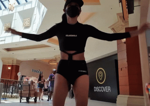 A Woman Wearing A Mask Is Standing In Front Of A Sign That Says Discover GIF