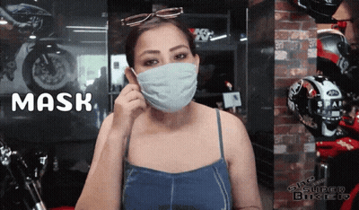 A Woman Wearing A Mask Is Standing In Front Of A Sign That Says Mask GIF