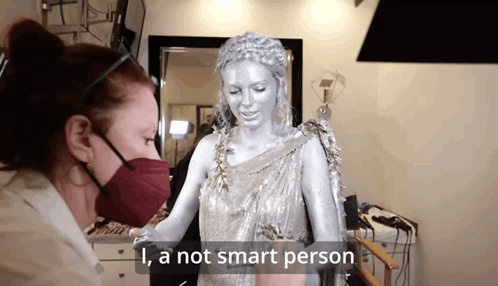 A Woman Wearing A Mask Is Standing Next To A Statue That Says " I 'M A Not Smart Person " GIF