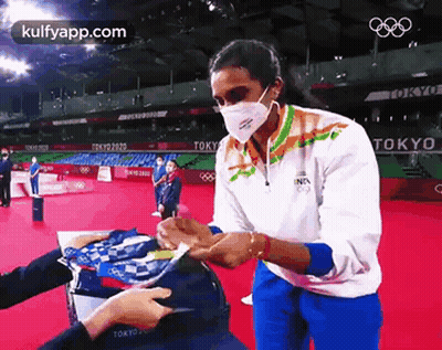 A Woman Wearing A Mask Is Standing On A Red Carpet And Signing A Hat . GIF