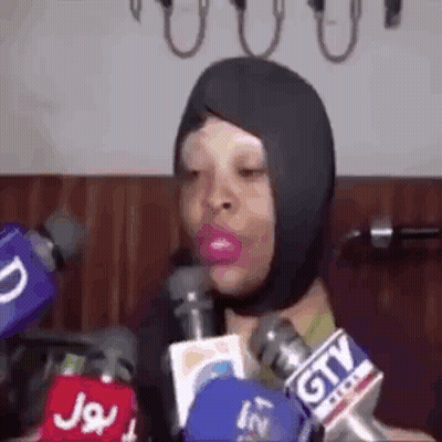 A Woman Wearing A Mask Is Talking Into Microphones . GIF