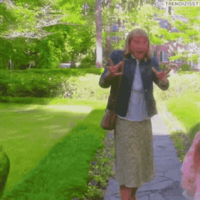 A Woman Wearing A Mask Is Walking Down A Path In The Park . GIF