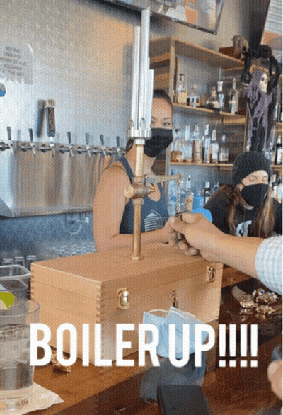 A Woman Wearing A Mask Stands Behind A Wooden Box That Says " Boiler Up " GIF
