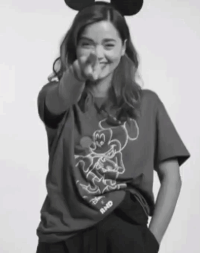 A Woman Wearing A Mickey Mouse T-Shirt Is Pointing GIF