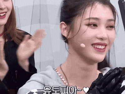 A Woman Wearing A Microphone And Gloves Is Smiling With A Heart In The Lower Right Corner GIF