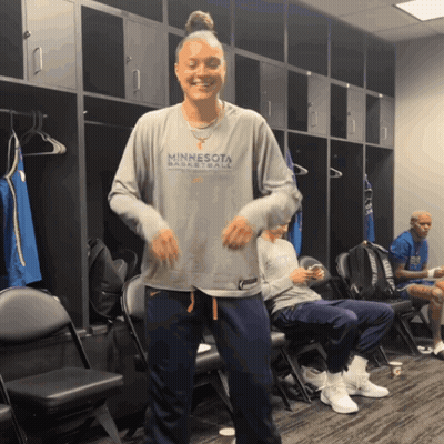 A Woman Wearing A Minnesota Basketball Shirt Is Dancing In A Locker Room GIF