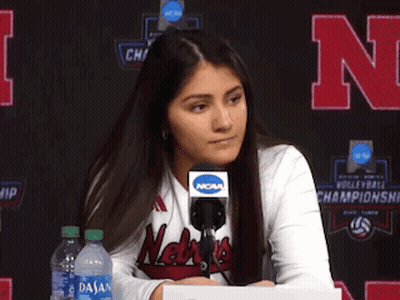 A Woman Wearing A Nebraska Shirt Is Sitting At A Desk With A Microphone GIF