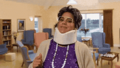 A Woman Wearing A Neck Brace And Glasses Is Giving A Thumbs Up In A Living Room . GIF