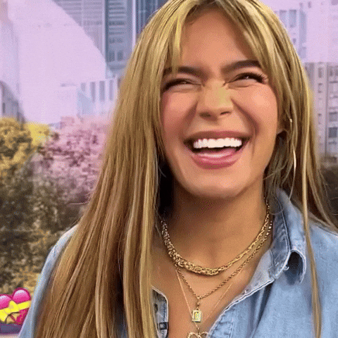 A Woman Wearing A Necklace And A Denim Shirt Is Smiling . GIF