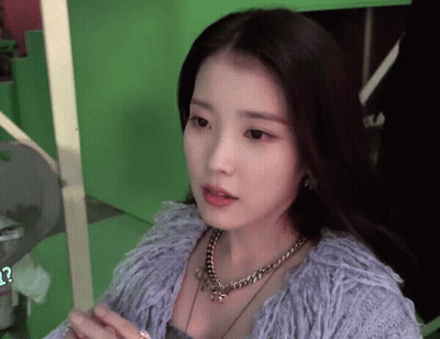 A Woman Wearing A Necklace And A Purple Sweater Looks At The Camera GIF