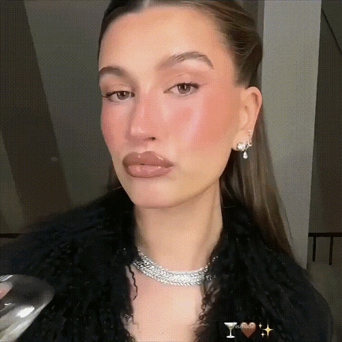 A Woman Wearing A Necklace And Earrings Holds A Glass Of Wine In Her Hand GIF