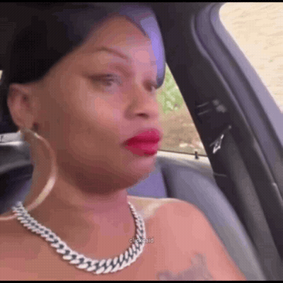 A Woman Wearing A Necklace And Earrings Is Sitting In A Car Making A Funny Face . GIF