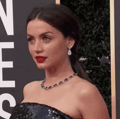 A Woman Wearing A Necklace And Earrings Is Standing In Front Of A Sign That Says ' N ' On It GIF
