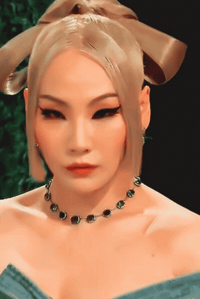 A Woman Wearing A Necklace And Earrings Looks At The Camera GIF