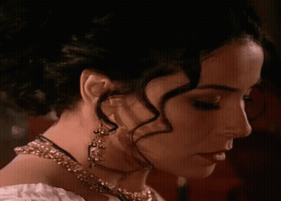A Woman Wearing A Necklace And Earrings Looks Down At Something GIF