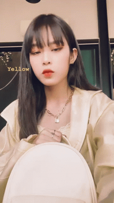 A Woman Wearing A Necklace With A Padlock On It Is Holding A White Backpack And Has The Word Yellow Written On Her Face GIF