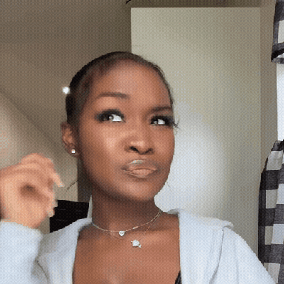 A Woman Wearing A Necklace With A Planet On It Looks At The Camera GIF