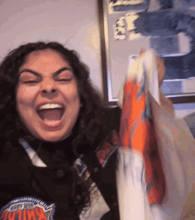 A Woman Wearing A New York Knicks Sweatshirt Is Holding A Bag GIF