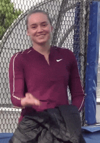 A Woman Wearing A Nike Shirt Is Smiling And Holding A Black Jacket GIF