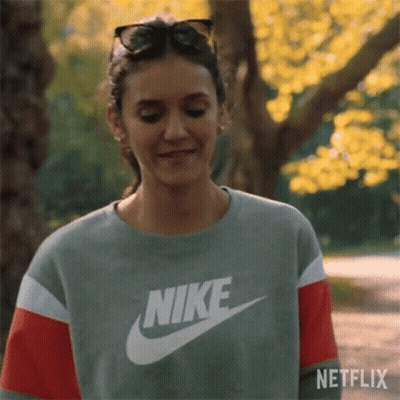 A Woman Wearing A Nike Sweatshirt And Sunglasses Is Smiling In A Park . GIF