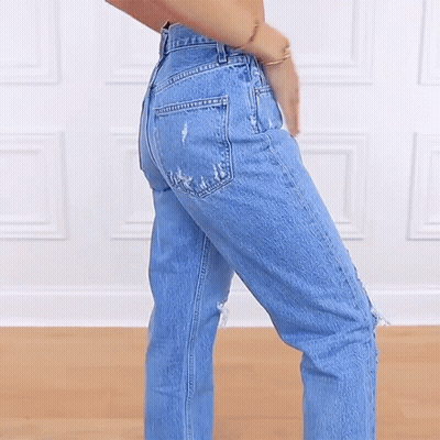 A Woman Wearing A Pair Of Ripped Jeans Stands With Her Hands In Her Pockets GIF