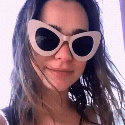 A Woman Wearing A Pair Of White Cat Eye Sunglasses Looks At The Camera GIF