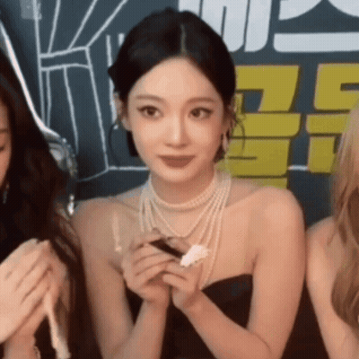 A Woman Wearing A Pearl Necklace And A Black Dress Is Holding A Piece Of Paper . GIF