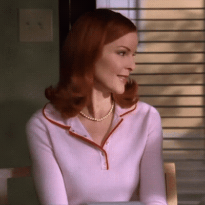 A Woman Wearing A Pearl Necklace And A Pink Shirt GIF