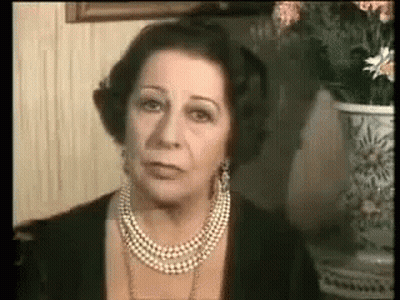 A Woman Wearing A Pearl Necklace And Earrings Is Looking At The Camera . GIF