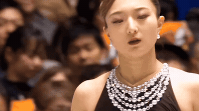 A Woman Wearing A Pearl Necklace And Earrings Is Standing In Front Of A Crowd GIF