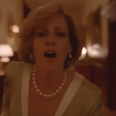 A Woman Wearing A Pearl Necklace And Gloves Is Standing On A Red Carpet In A Room . GIF