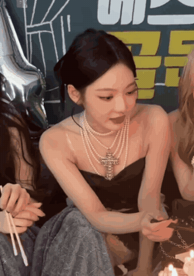 A Woman Wearing A Pearl Necklace Is Sitting Next To A Cake With Candles GIF