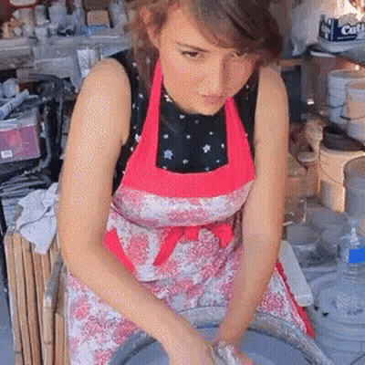 A Woman Wearing A Pink Apron Is Working On A Pottery Wheel In Front Of A Box That Says Citi GIF