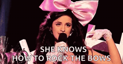 A Woman Wearing A Pink Bow Is Holding A Microphone And Talking Into It . GIF