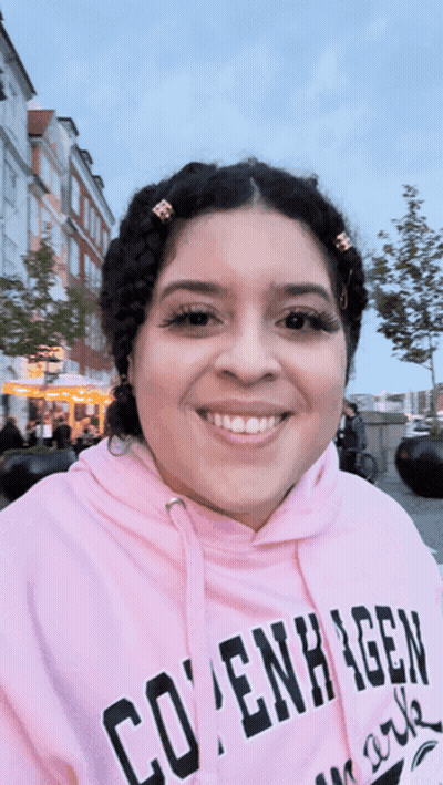 A Woman Wearing A Pink Copenhagen Hoodie Smiles GIF
