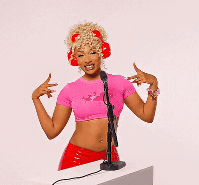 A Woman Wearing A Pink Crop Top And Red Headphones Is Standing In Front Of A Microphone GIF