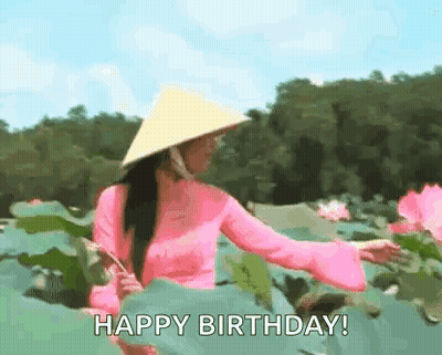 A Woman Wearing A Pink Dress And A Conical Hat Is Standing In A Field Of Water Lilies . GIF