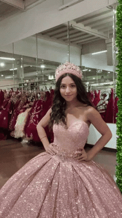 A Woman Wearing A Pink Dress And A Crown Is Standing In Front Of A Mirror GIF