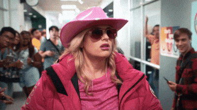 A Woman Wearing A Pink Hat And Sunglasses Is Walking Down A Hallway . GIF