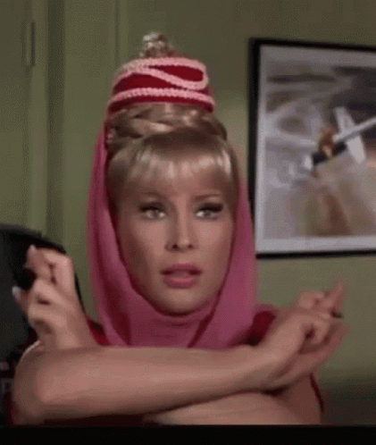 A Woman Wearing A Pink Head Scarf And A Red Hat Is Sitting In A Room . GIF