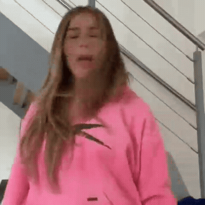 A Woman Wearing A Pink Hoodie Is Standing On A Staircase . GIF