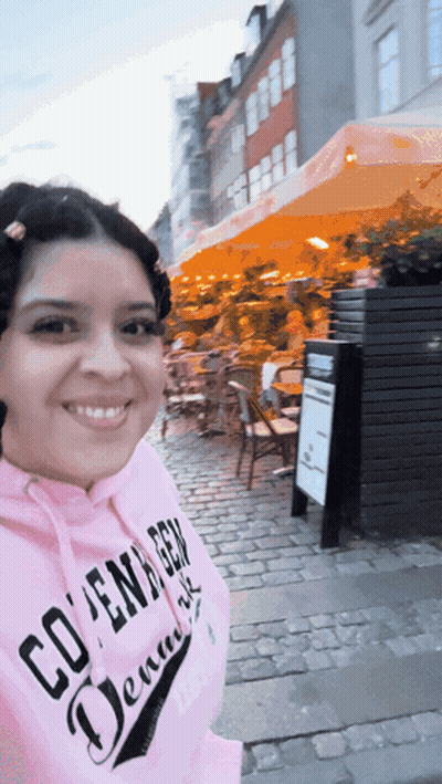 A Woman Wearing A Pink Hoodie That Says Copenhagen Denmark Is Smiling GIF