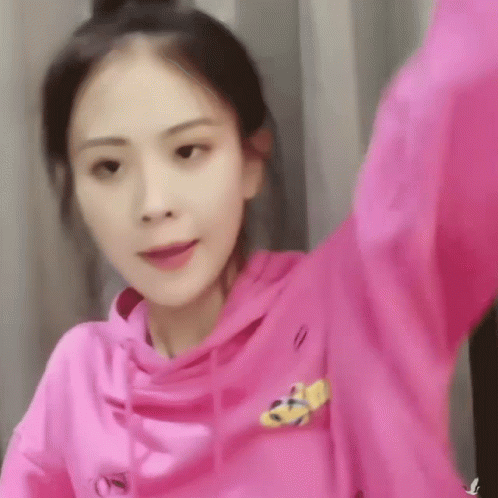 A Woman Wearing A Pink Hoodie With A Yellow Logo On The Front GIF
