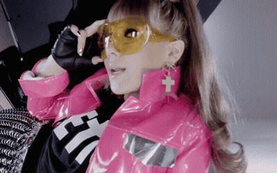 A Woman Wearing A Pink Jacket And Yellow Sunglasses Has A Cross On Her Earring GIF
